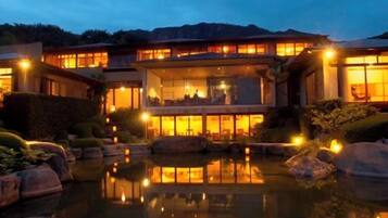 A multi-story building with a reflective pool in front, surrounded by rocks and plants.