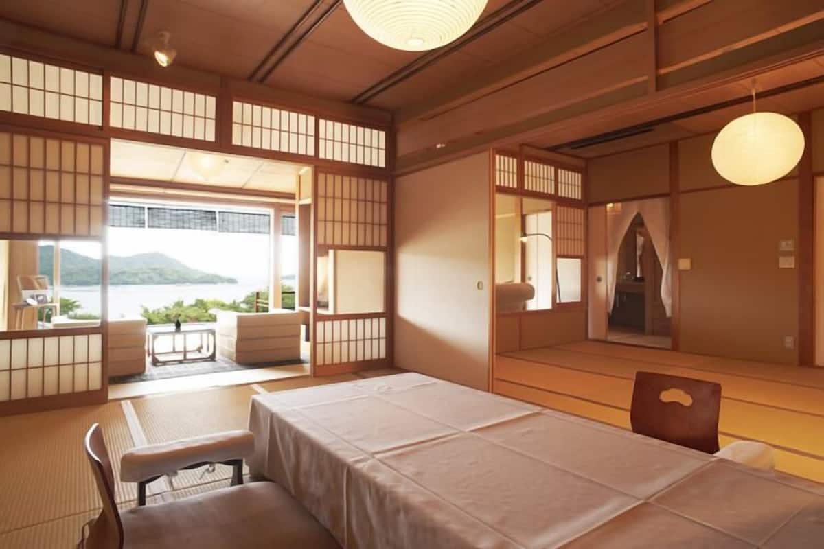 A traditional Japanese room with tatami flooring, a low table, and a bed with a white bedspread.