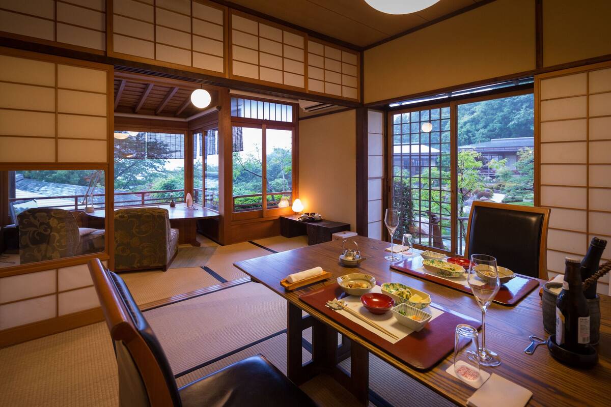A traditional Japanese room with tatami flooring, a low table, and a view of greenery outside.