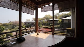 A room with a wooden table, a clock, and a view of a garden and buildings outside.