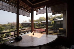 Ein Zimmer mit einem Holztisch, einer Uhr und Blick auf einen Garten sowie Gebäude.