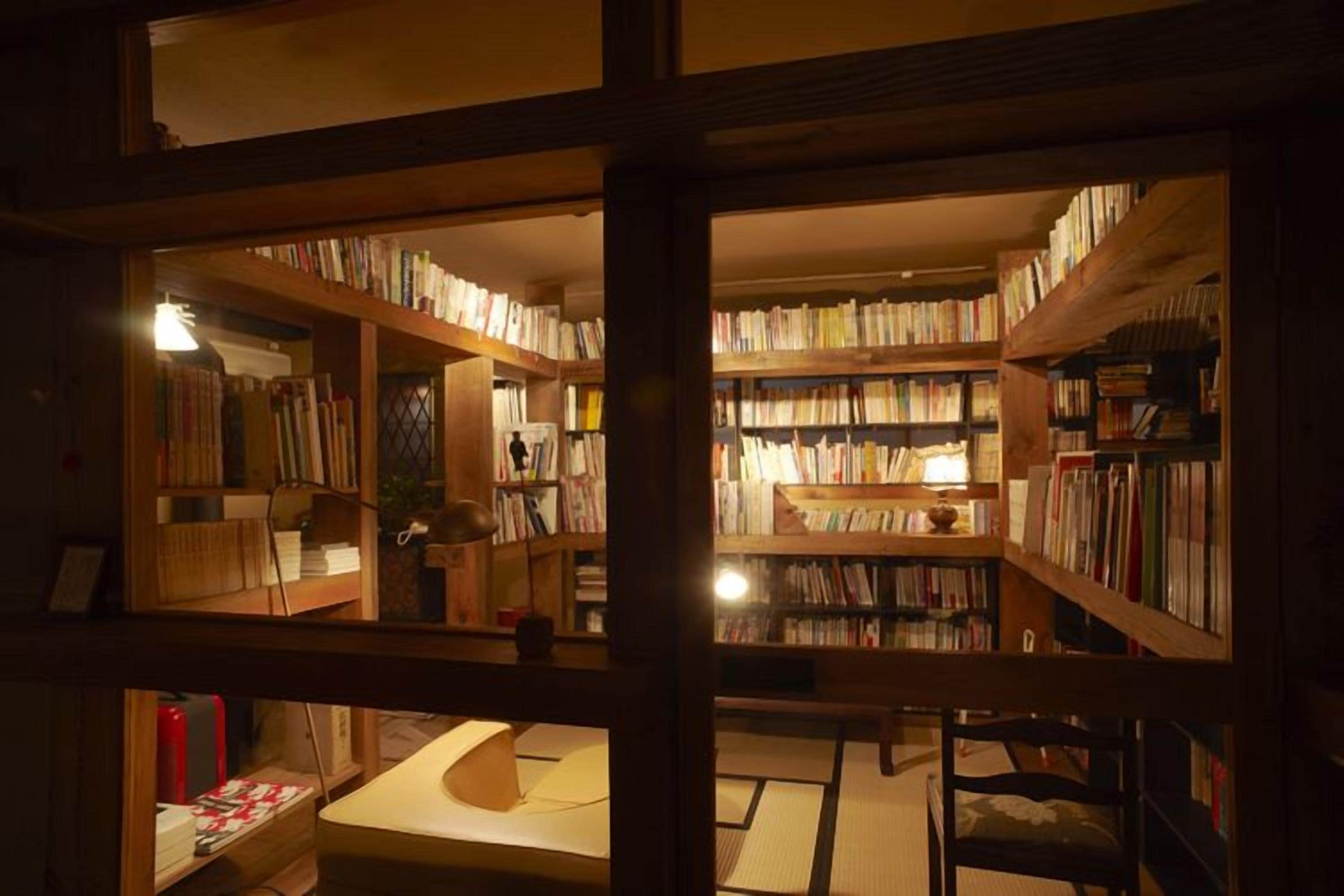Une bibliothèque avec des étagères, un espace lecture et une petite table avec une lampe.