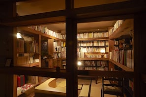 A library with bookshelves, a reading area, and a small table with a lamp. - Miyahama Onsen Teien no Yado Sekitei (Hatsukaichi)
