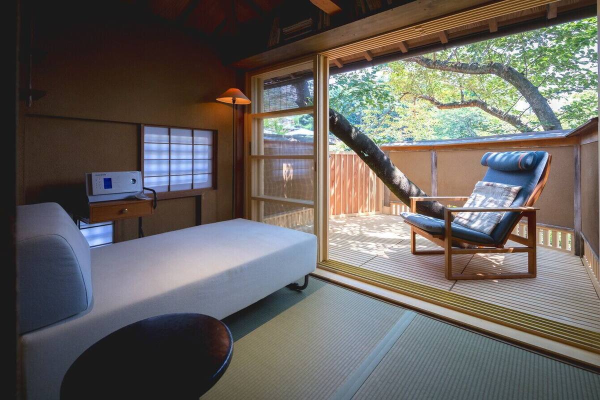 A room with a bed, a desk, a chair, and a large window with a view of trees.