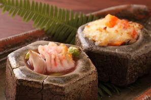 A rustic wooden table with two dishes, one with shrimp and the other with a cheese topping. - Miyahama Onsen Teien no Yado Sekitei (Hatsukaichi)