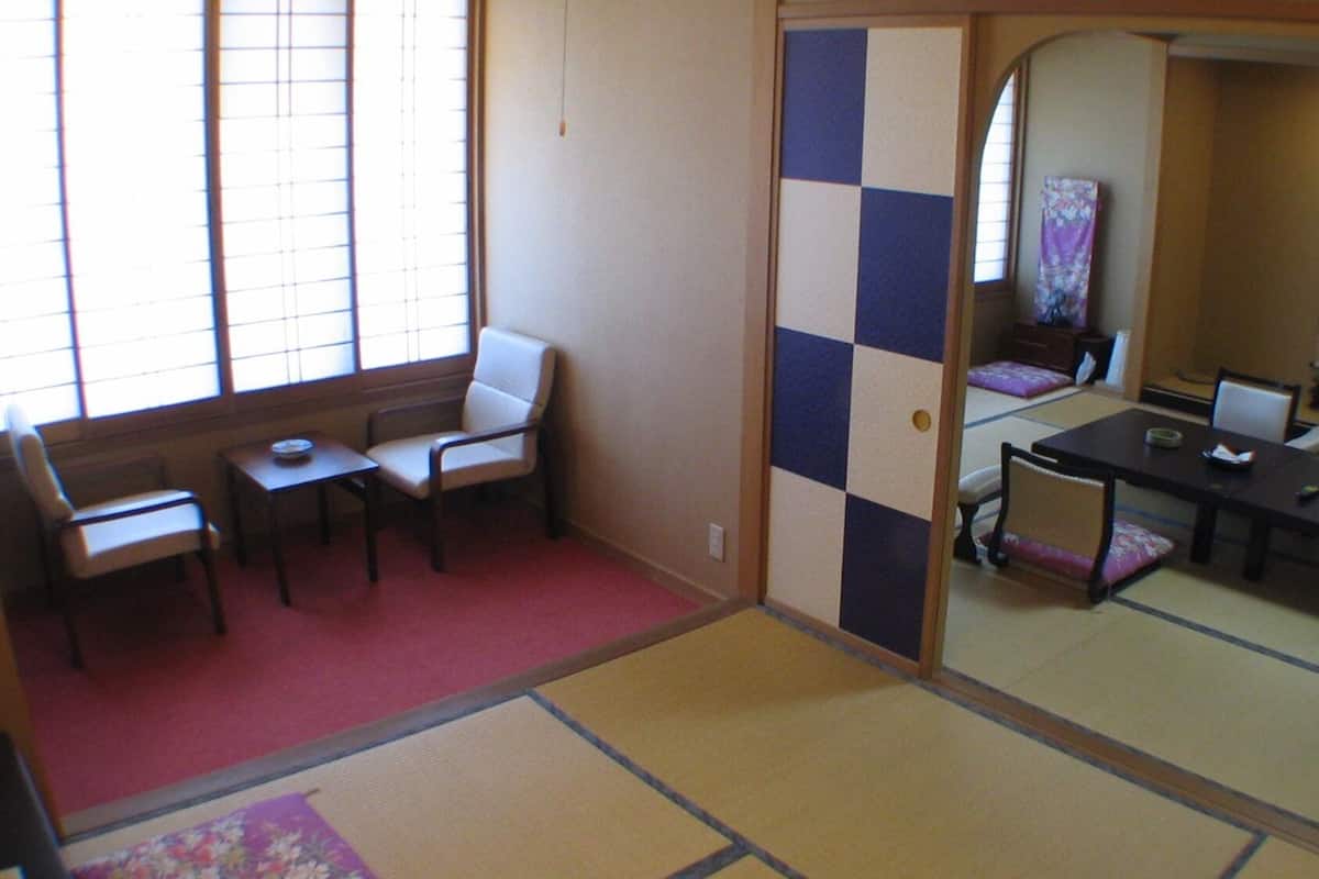 A traditional Japanese room with tatami flooring, a low table with a cushion, a chair, and a sliding door leading to another room.