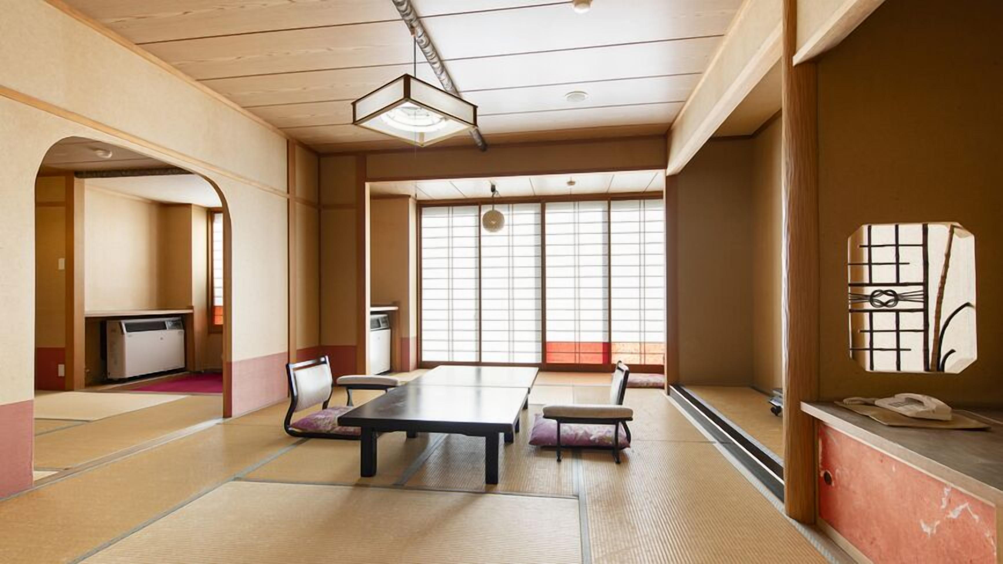 A traditional Japanese room with tatami flooring, a low table, chairs, a desk, and a sliding door.