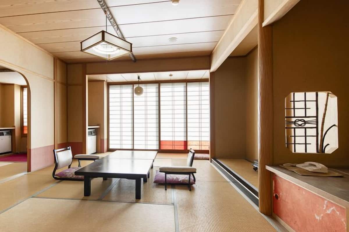 A traditional Japanese room with tatami flooring, a low table, chairs, a desk, and a sliding door.