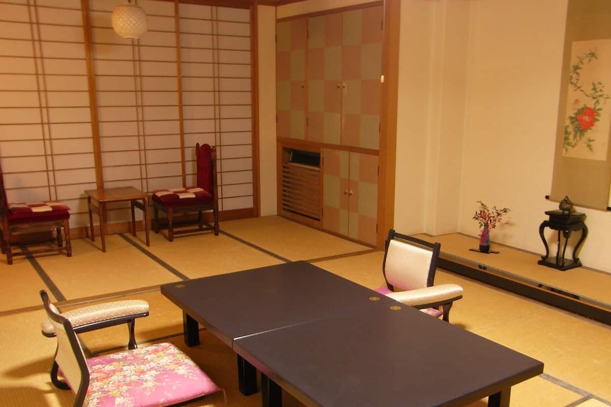 A traditional Japanese room with tatami flooring, a low table, two chairs, a cabinet, and a vase with flowers.
