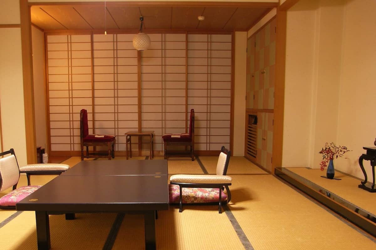 A traditional Japanese room with tatami flooring, a low table, and two chairs.