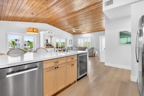 A modern kitchen with wooden ceiling beams, a stainless steel refrigerator, and a dishwasher. - Paloma | Canalfront Key Largo Home, Dock, Pool, Porch, Walkable (Key Largo)