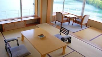 A tatami mat room with a low table, two chairs, and a view of a river.