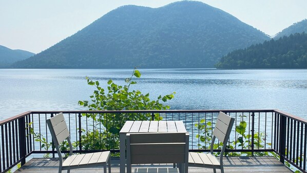 A wooden deck with a table and two chairs, overlooking a calm lake with mountains in the background. - Shikaribetsu-kohan Onsen Hotel Fuusui (Shikaoi)