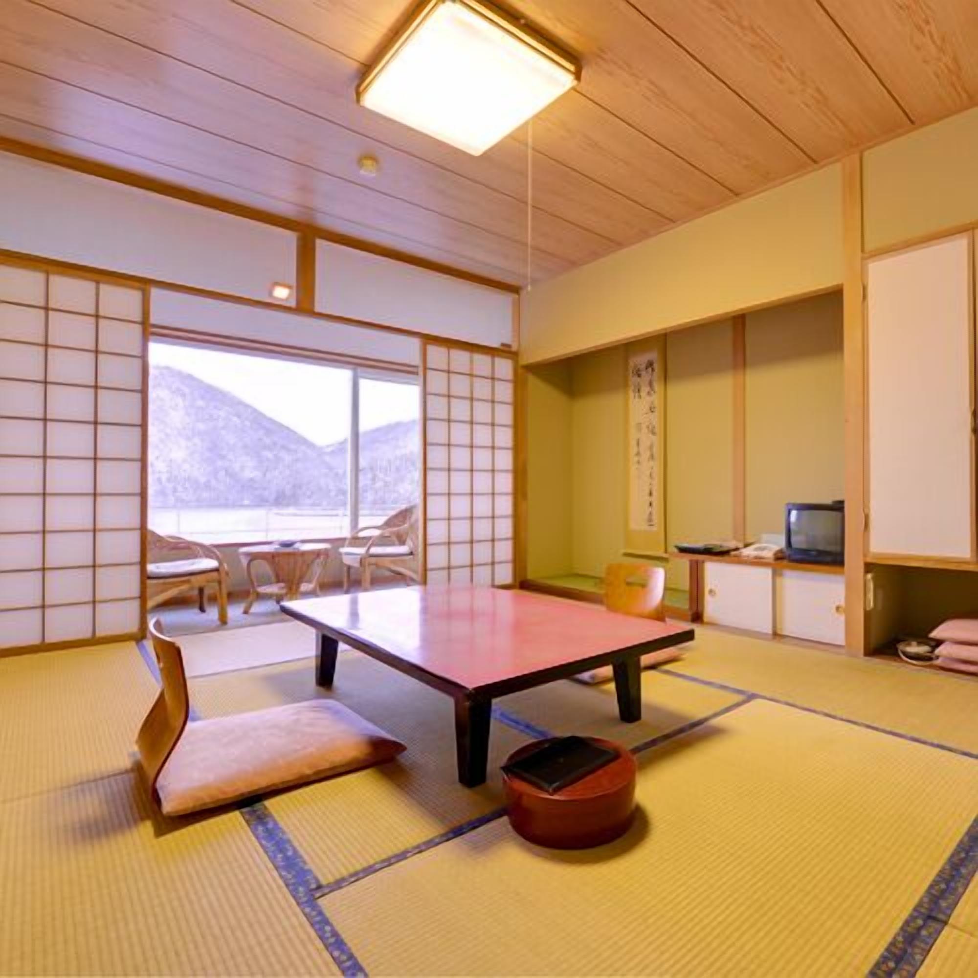 Ein Raum mit Tatami-Matten, einem niedrigen Tisch, Kissen und einem Fernseher.