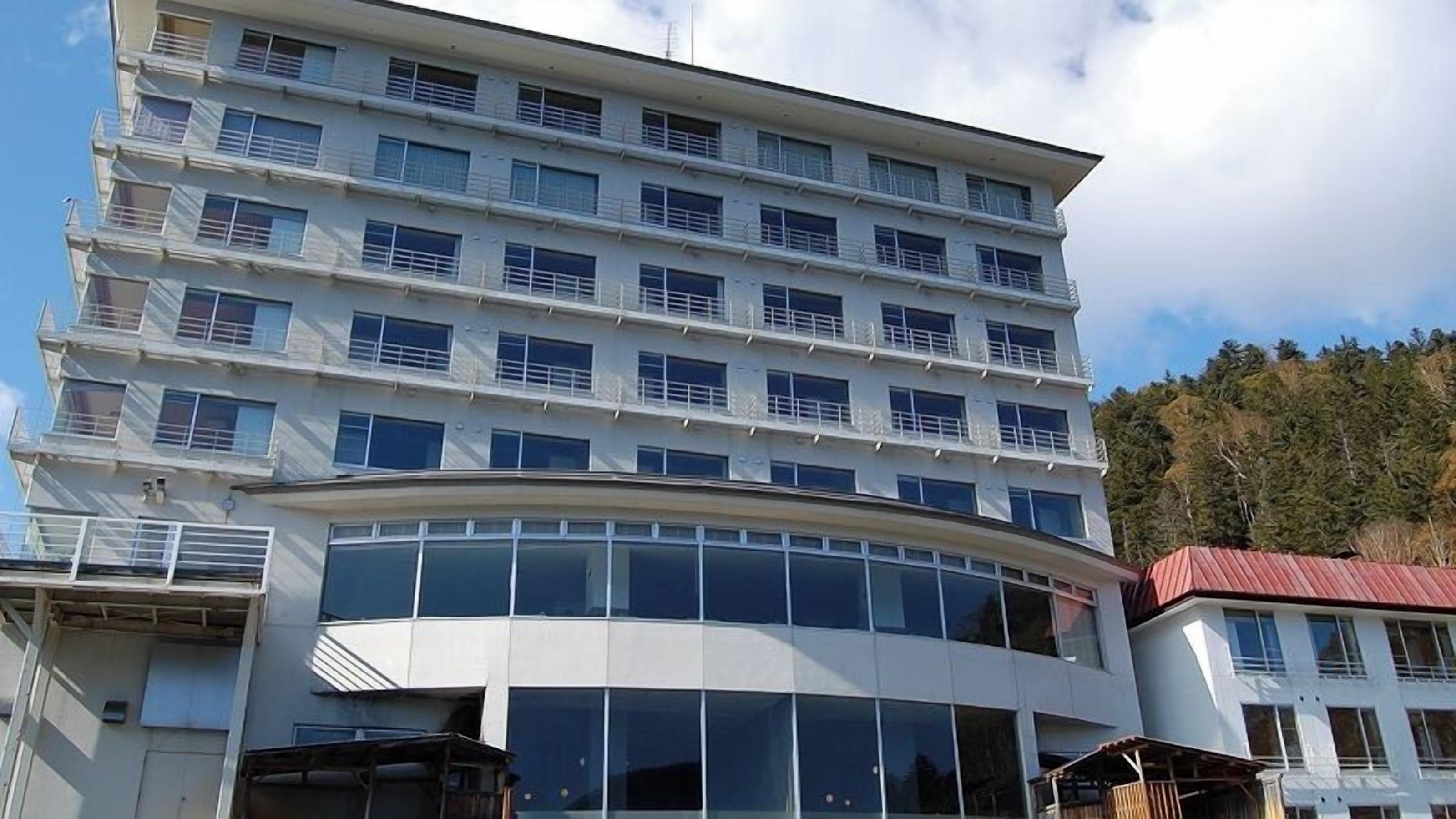 A multi-story hotel with a curved glass facade, balconies, and a red-roofed structure adjacent to it.