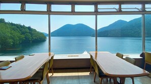 A dining area with tables and chairs, large windows with a view of a lake and mountains. - Shikaribetsu-kohan Onsen Hotel Fuusui (Shikaoi)