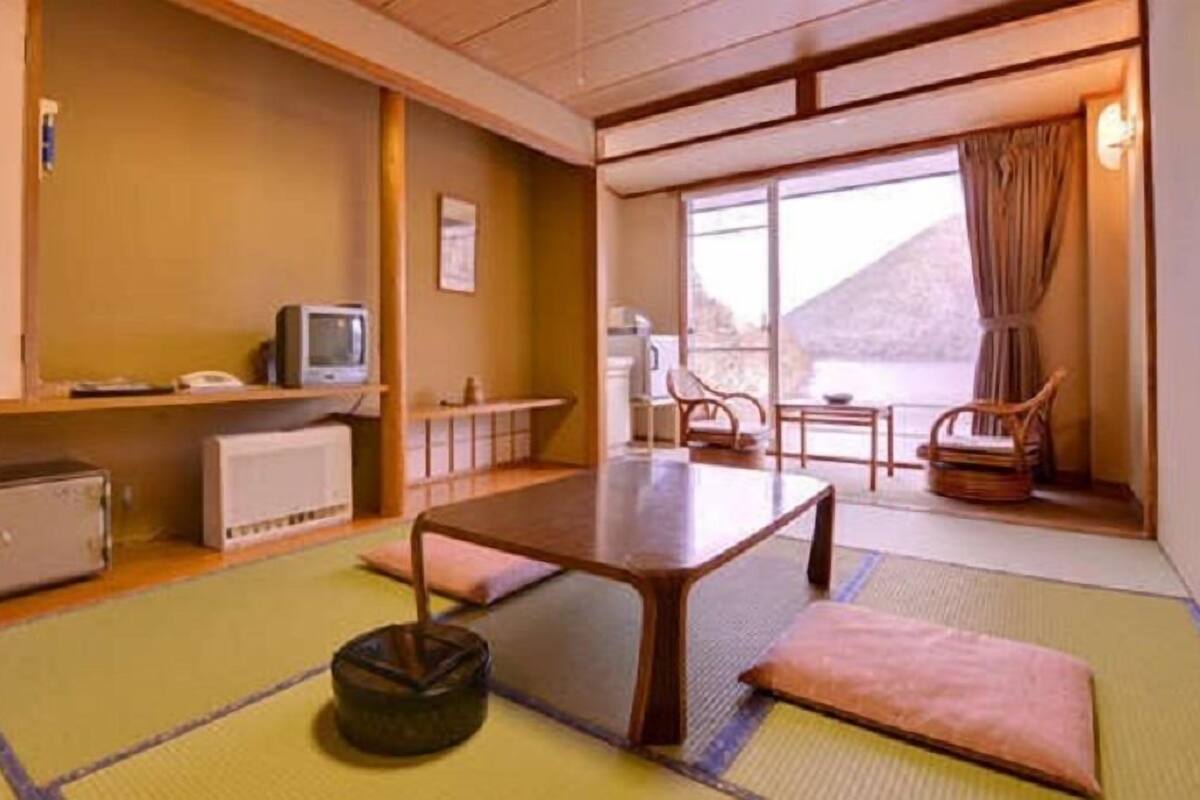 Una habitación japonesa tradicional con suelo de tatami, una mesa baja, un televisor y vistas a la montaña.