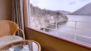 A room with a view of a lake and mountains, a wicker chair, a small table with a tissue and a remote control, and a window with a curtain. - Shikaribetsu-kohan Onsen Hotel Fuusui (Shikaoi)