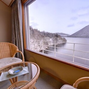 A room with a view of a lake and mountains, a wicker chair, a small table with a tissue and a remote control, and a window with a curtain. - Shikaribetsu-kohan Onsen Hotel Fuusui (Shikaoi)