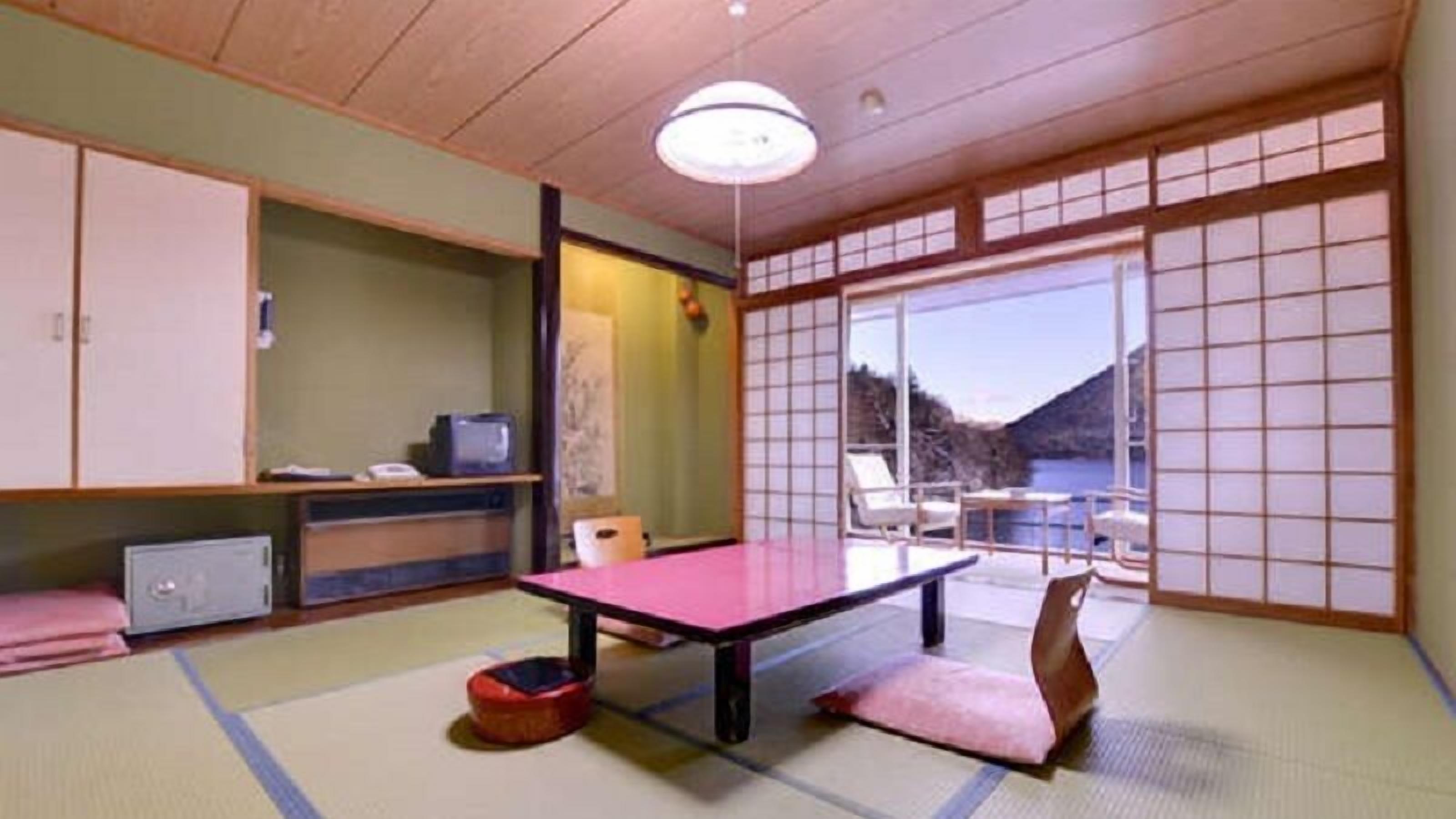 Perinteinen japanilainen huone, jossa on tatamimatto, futon-patja, matala pöytä ja liukuovet, jotka johtavat parvekkeelle, jolta on näkymä.