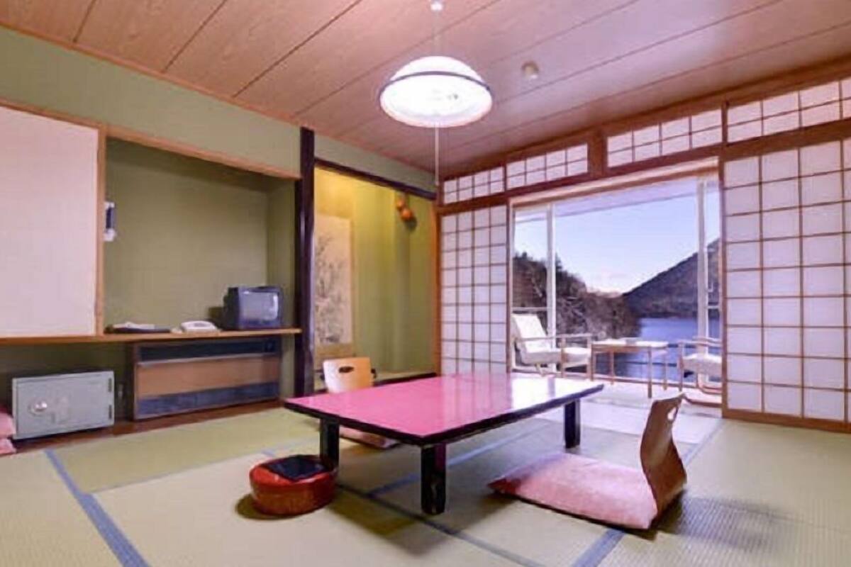 Una habitación japonesa tradicional con suelo de tatami, un futón, una mesa baja y puertas correderas que dan a un balcón con vistas.