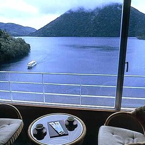 A room with a large window overlooking a body of water and a boat. There is a round table with a book and two cups. - Shikaribetsu-kohan Onsen Hotel Fuusui (Shikaoi)