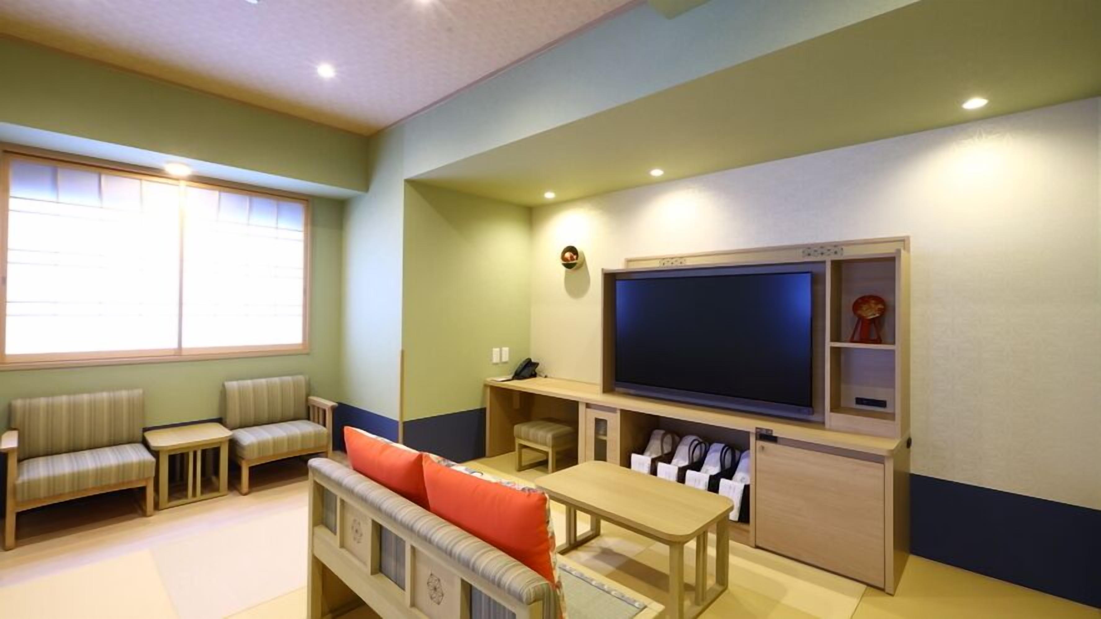 Ein Wohnzimmer mit Fernseher, Sitzgelegenheiten und einem Fenster.