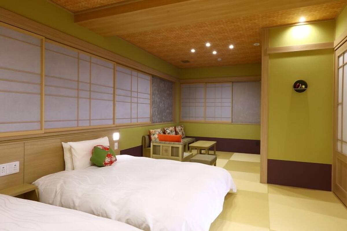 A hotel room with two beds, a small seating area, and a traditional Japanese-style sliding door.
