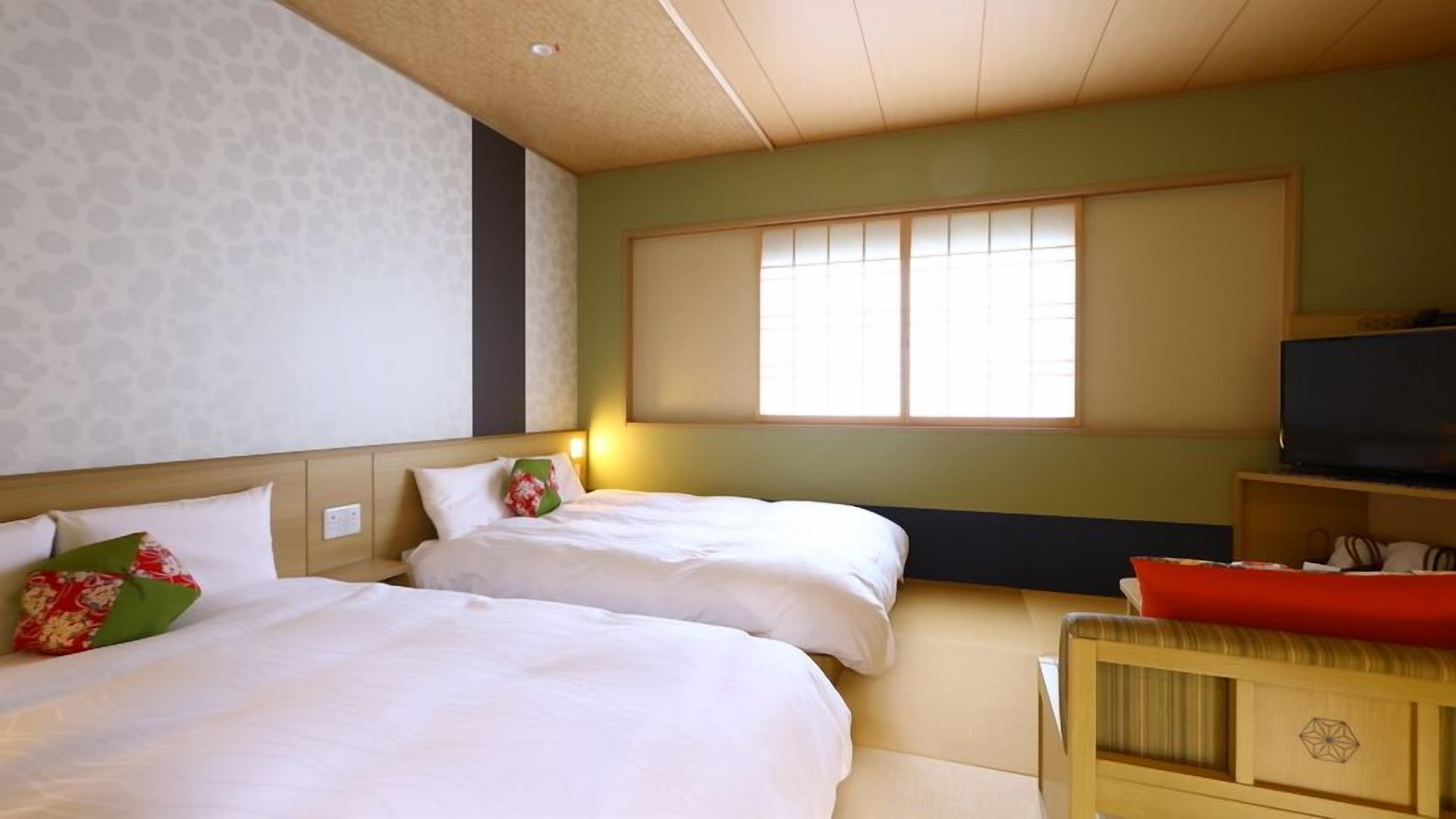 Ein Hotelzimmer mit zwei Betten, einem Fernseher und einem Fenster mit Jalousien.