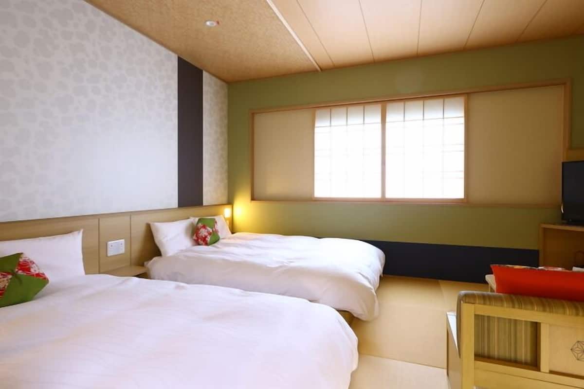 A hotel room with two beds, a television, and a window with blinds.