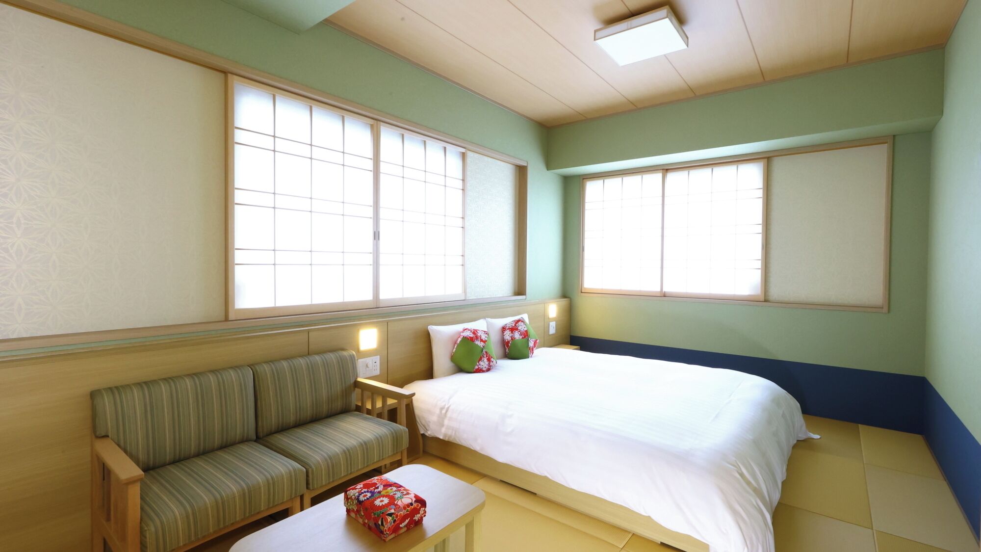 A room with a bed, a sofa, a small table, and two windows.