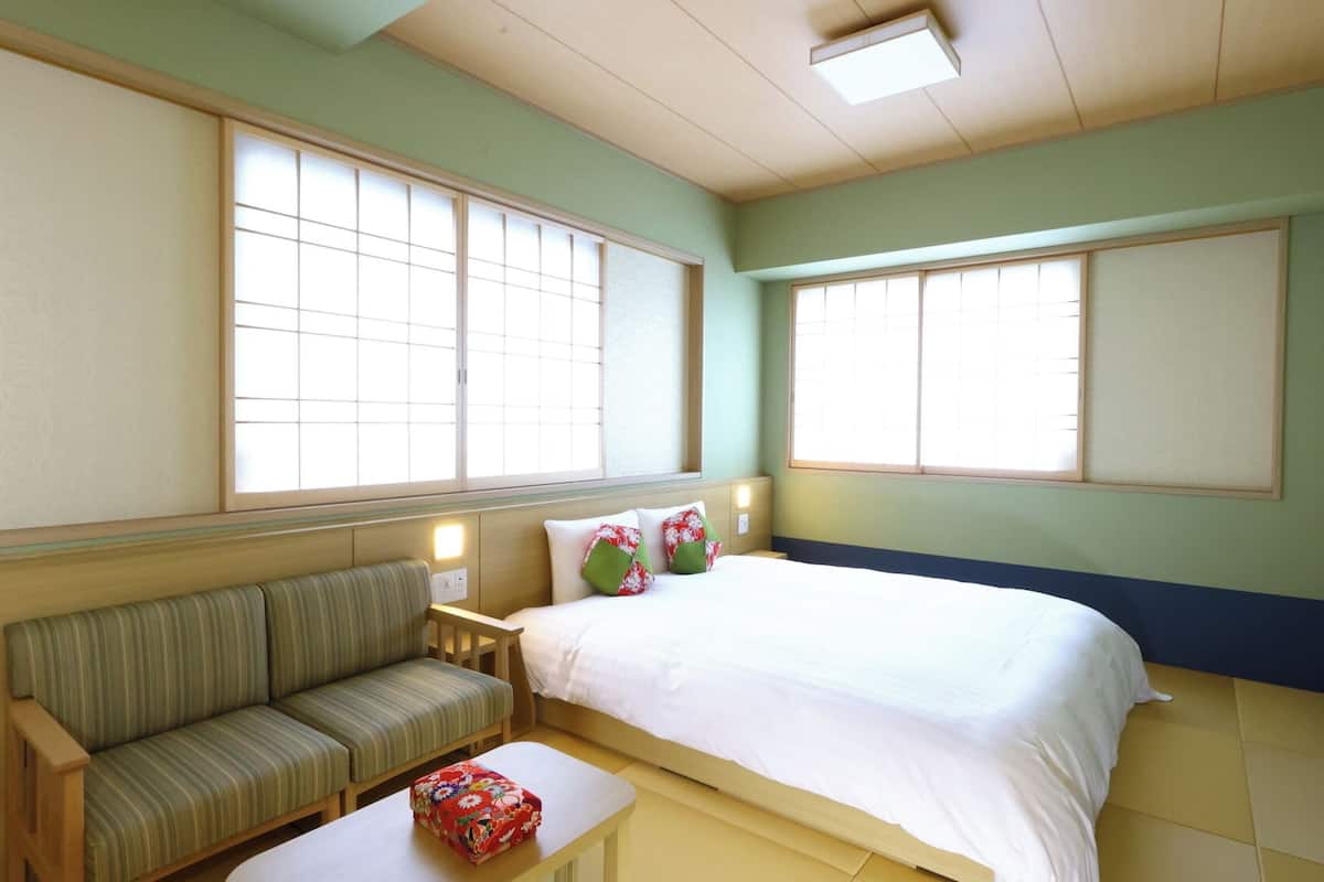 A room with a bed, a sofa, a small table, and two windows.