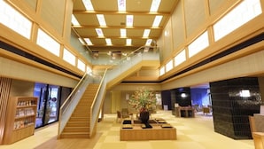 A spacious lobby with a central staircase, wooden flooring, and a seating area with a potted plant. - Dandan No Yu Onyado Nono Matsue (Matsue)