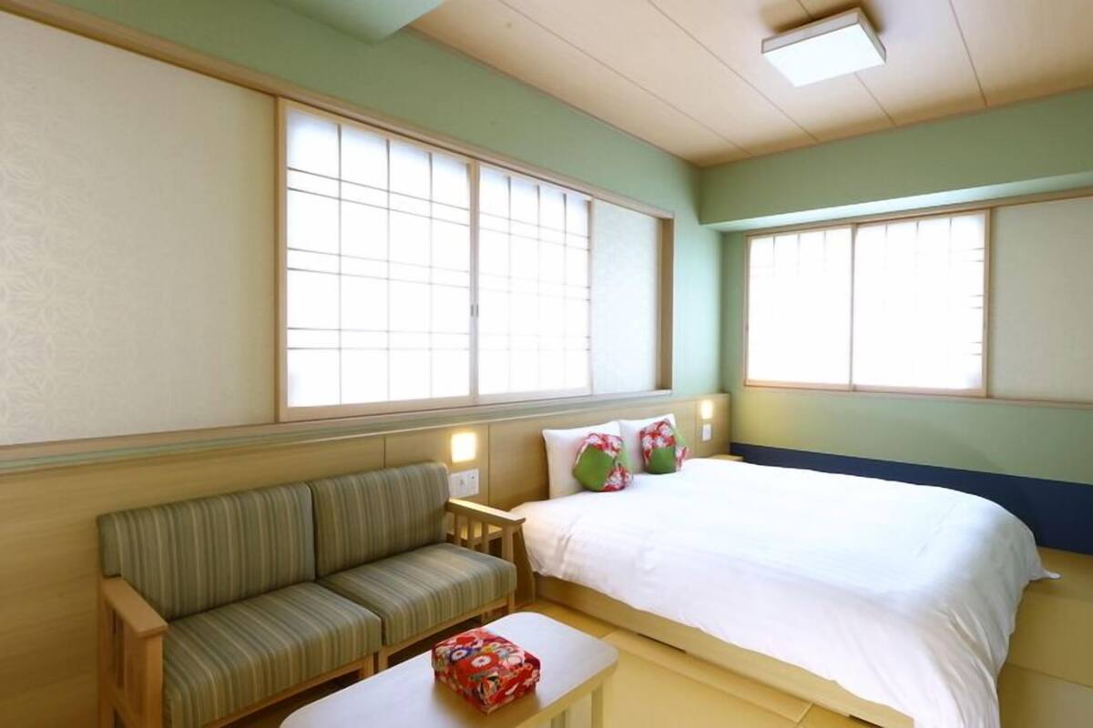 A room with a bed, a sofa, and two windows.