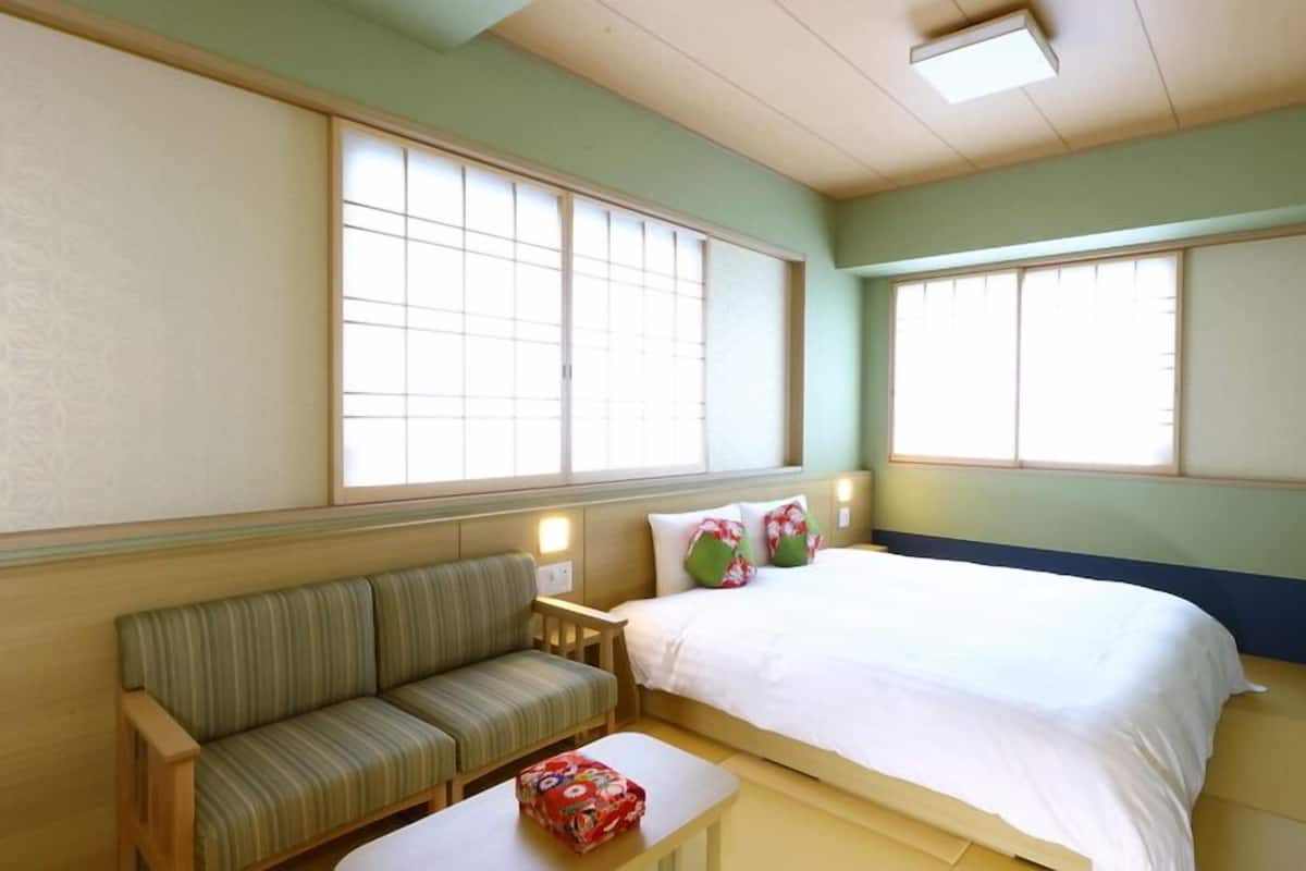 A room with a bed, a sofa, and two windows.