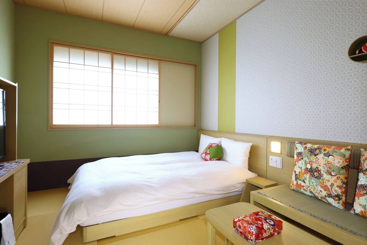 A hotel room with a bed, a desk, a chair, a small table, and a window.