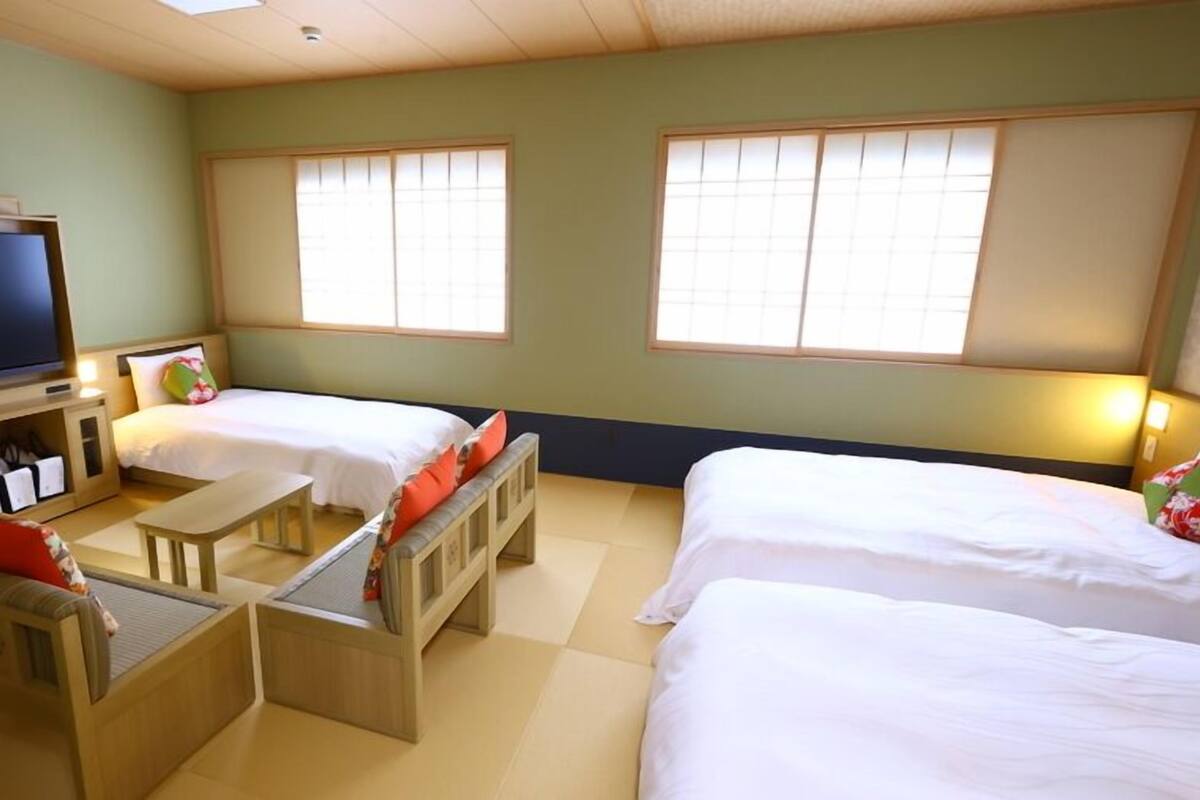 A hotel room with two beds, a TV, a small table, and a bench.
