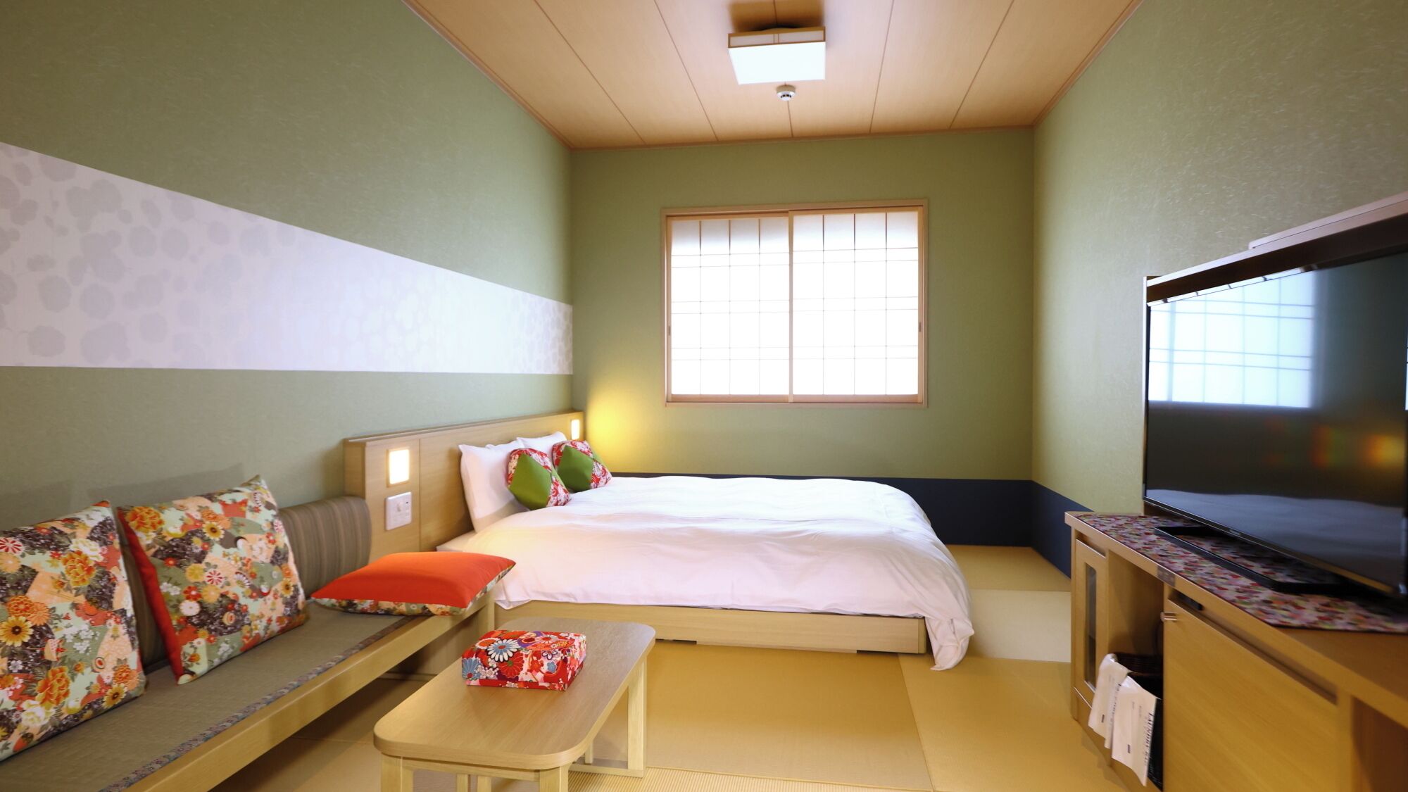 A hotel room with a bed, a sofa, a small table, a TV, and a window.