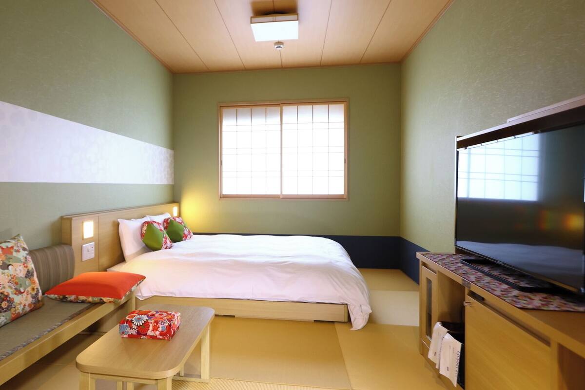 A hotel room with a bed, a sofa, a small table, a TV, and a window.