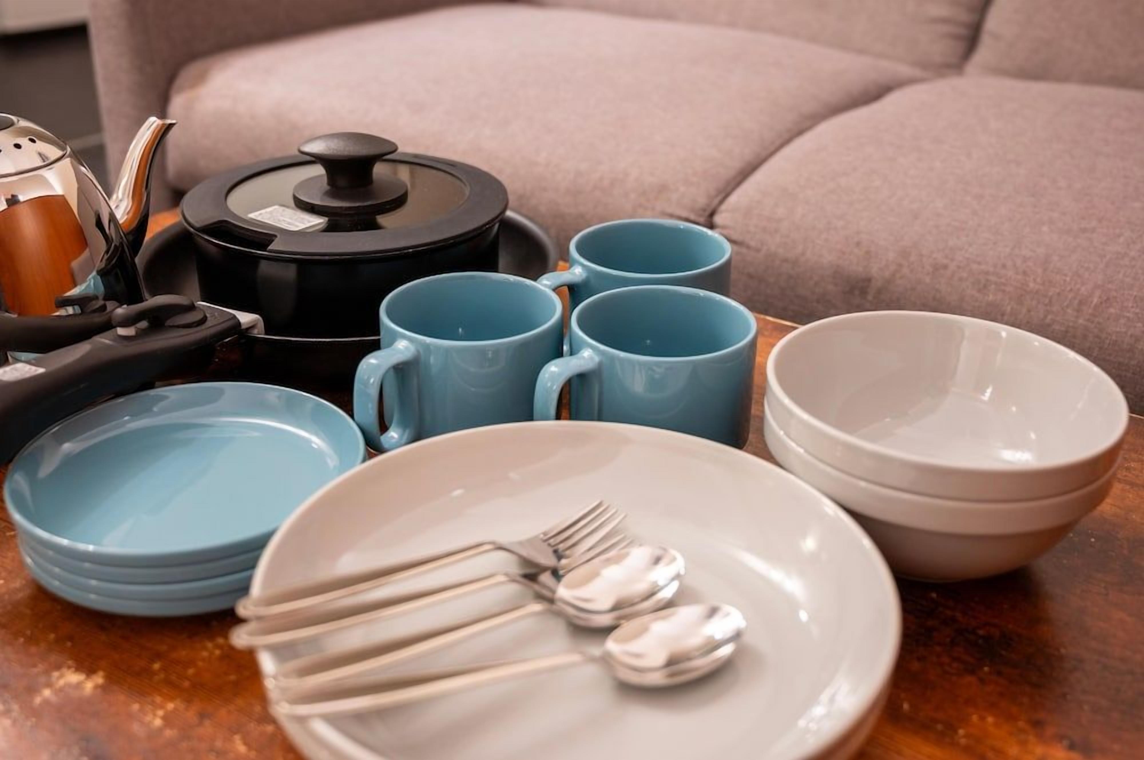 A dining setup with a coffee maker, mugs, plates, and cutlery on a table.