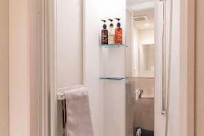 A bathroom with a glass shower enclosure, a towel rack, and a shelf with toiletries. - Coco Shuku Nakano (Tokyo)