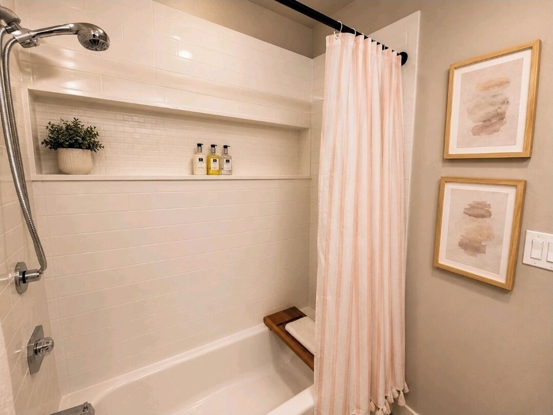A bathroom with a shower, a shelf with toiletries, and two framed pictures on the wall.