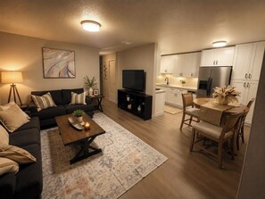 A living room with a sofa, coffee table, TV, and a kitchen area with cabinets and a refrigerator. - Beautiful 2-bedroom building in charming Sacramento (Sacramento)