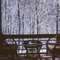 Habitación con un gran ventanal que da a un bosque nevado. En primer plano, hay dos sillones de mimbre y una mesita.