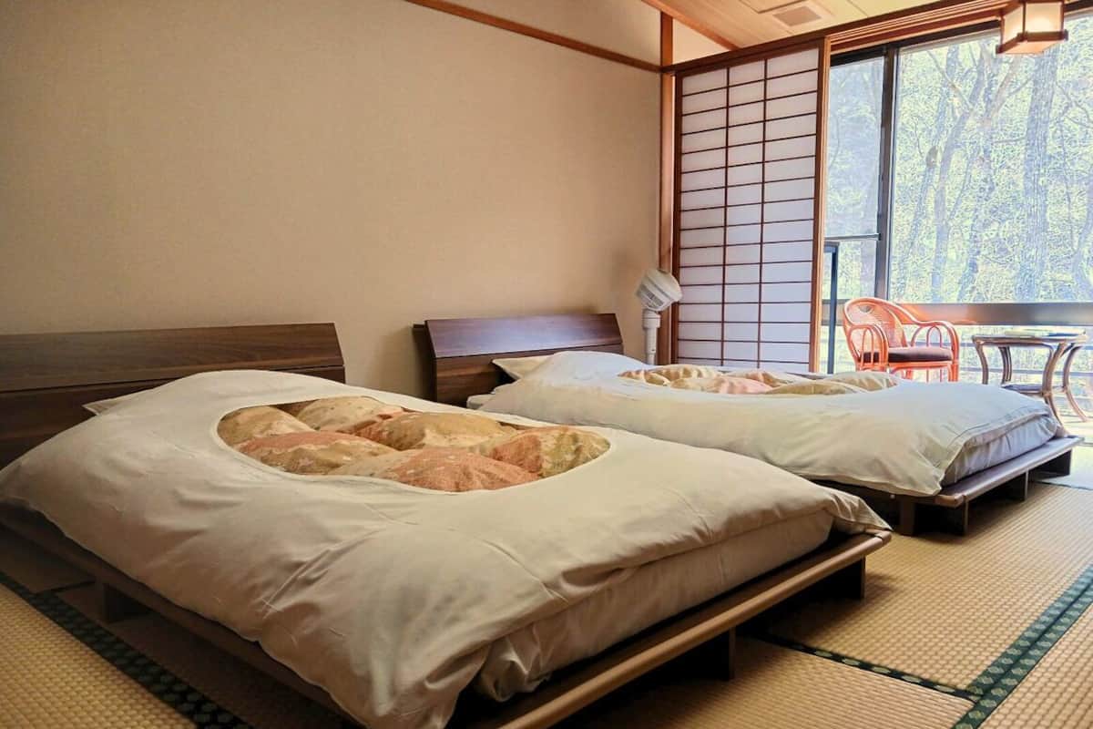 Zwei Betten mit Tatami-Matten, eine Schiebetür und Blick auf Bäume.