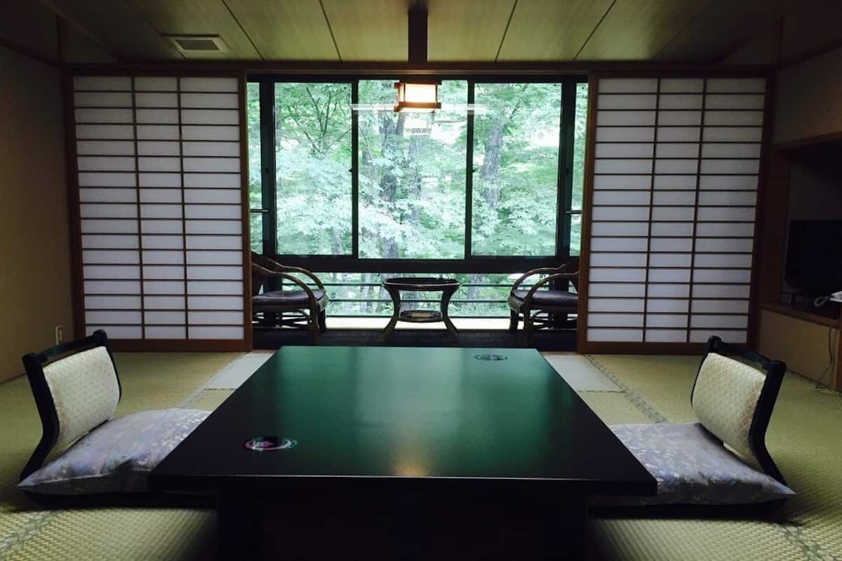 Ein Raum mit Tatami-Böden, einem niedrigen Tisch, Kissen und verschiebbaren Türen.