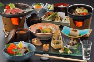 Variedad de platos japoneses y ollas calientes, incluyendo sashimi, verduras y tofu, sobre una mesa con palillos y un vaso de agua.