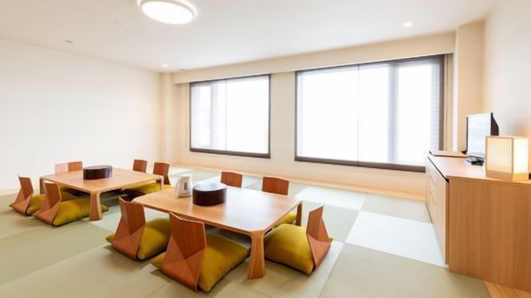 Une salle de conférence équipée de tables et de chaises, de grandes fenêtres et d’un bureau avec une lampe.