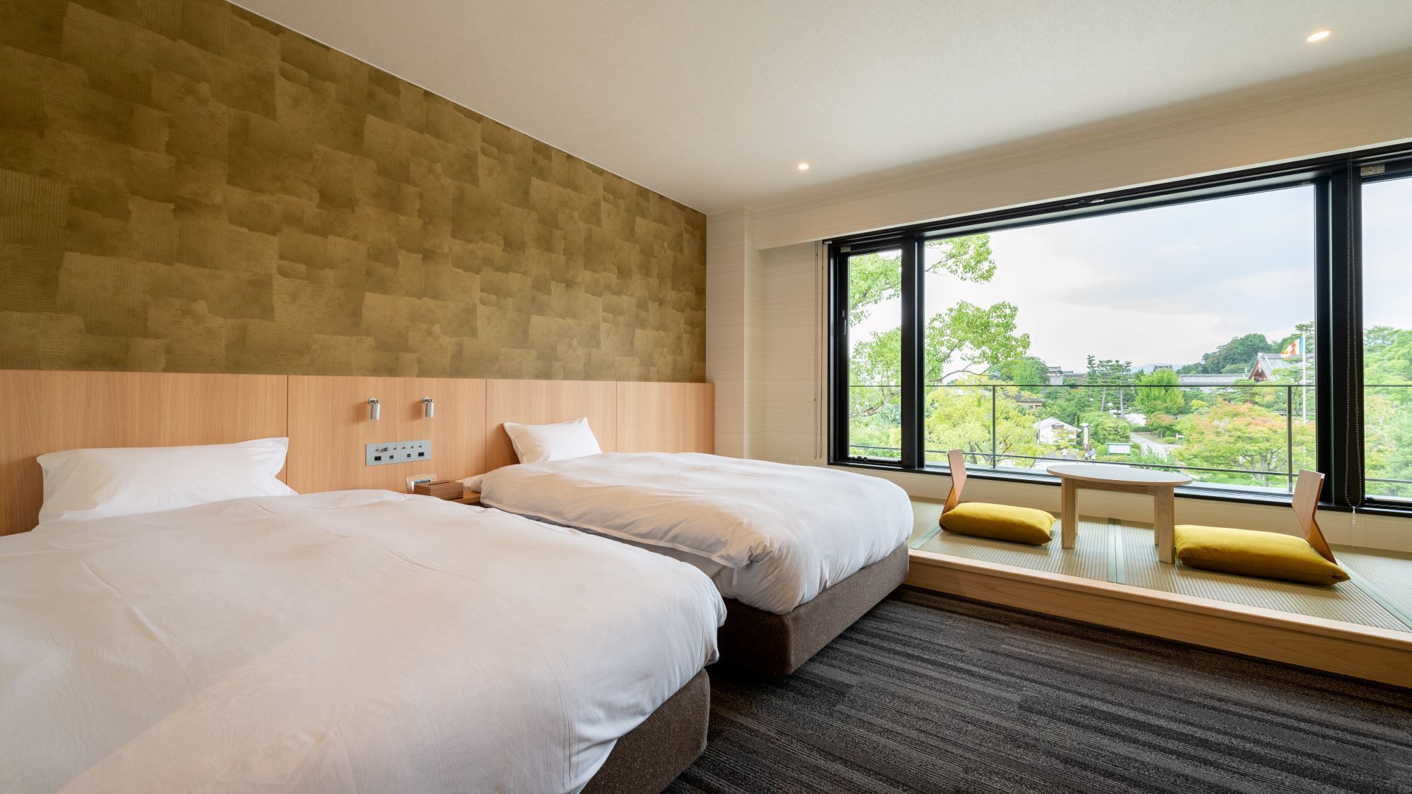 A modern hotel room with two beds, a large window with a view, and a small table.
