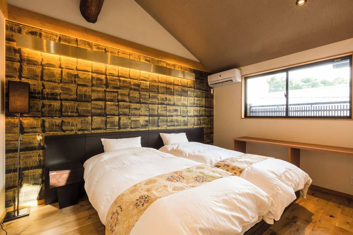 A hotel room with a brick-patterned headboard, a large window with a view, a bedside table, and a bed with white bedding.